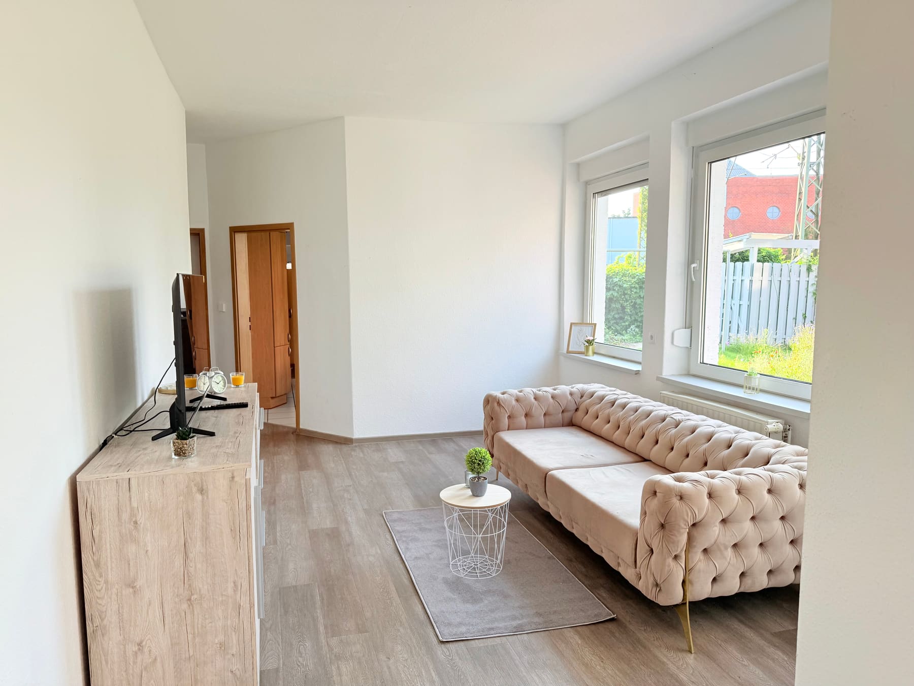 Helles Wohnzimmer mit Sofa, Fernseher und großen Fenstern